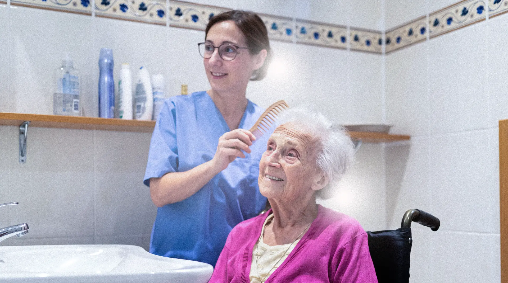 A caregiver gently combing an older woman’s hair as she sits in her wheelchair at home