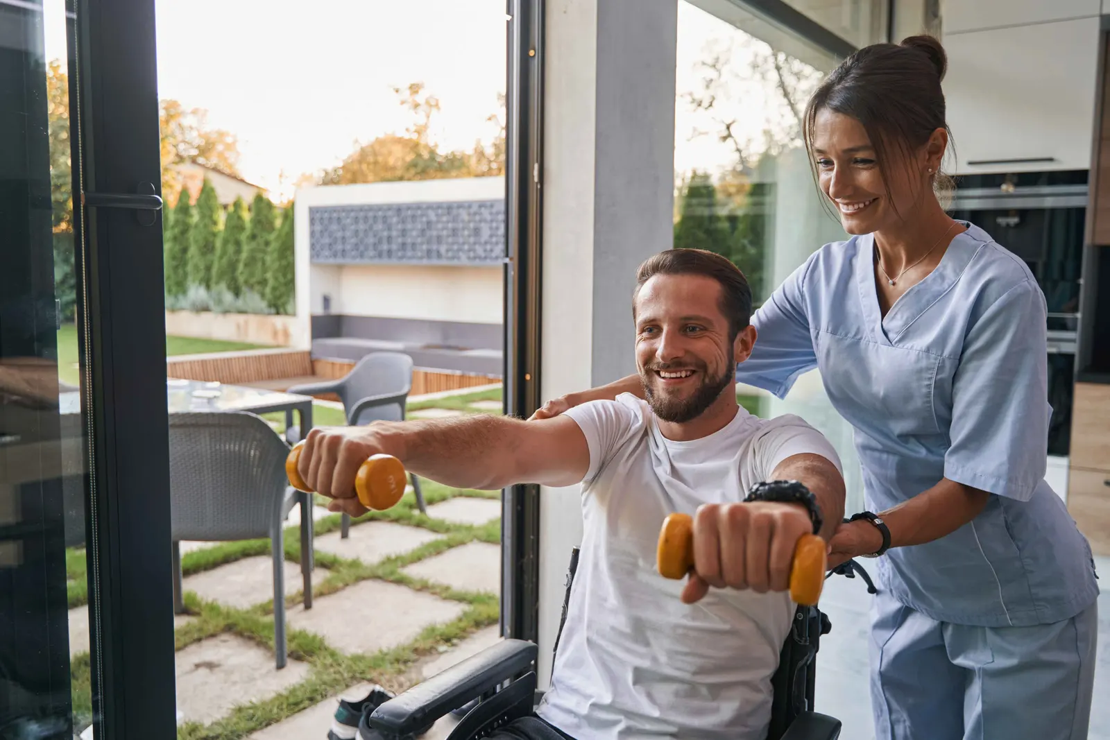 A nursing assistant steadying an older woman's hand as she stands up at home